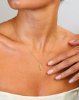 Necklace with a pendant worn by a person, with a hand touching the neck.
