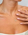 Gold necklace with a letter 'H' pendant on a person's neck with a hand touching the skin.