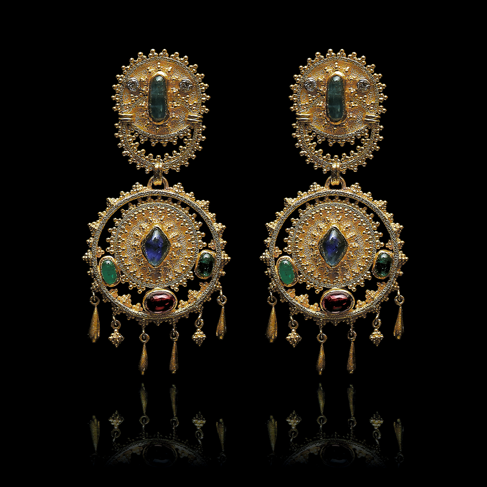 Ornate gold earrings with gemstones on a black background