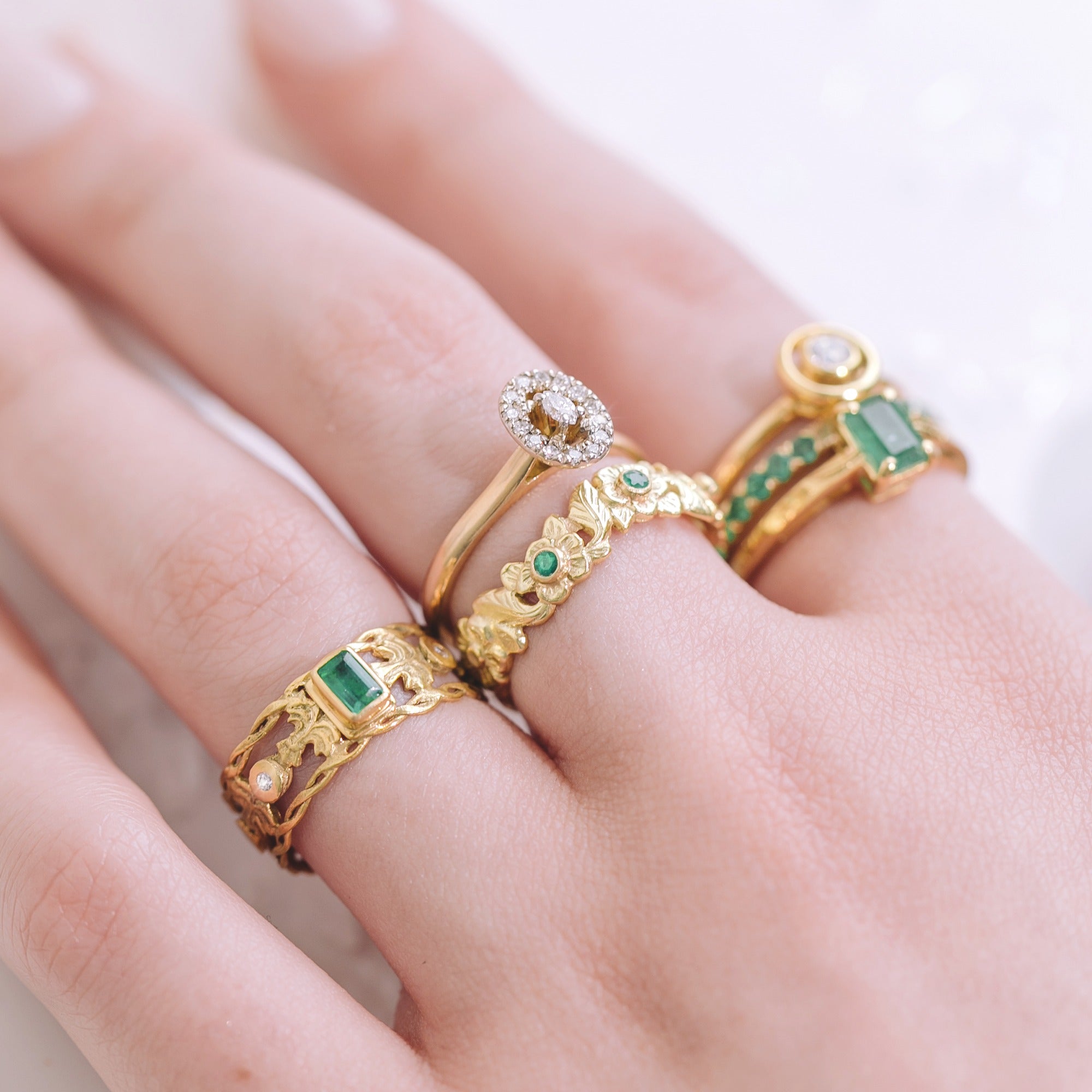Close-up of a hand wearing gold rings with emeralds and diamonds.