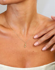 Woman wearing a gold necklace with a small pendant on a neutral background