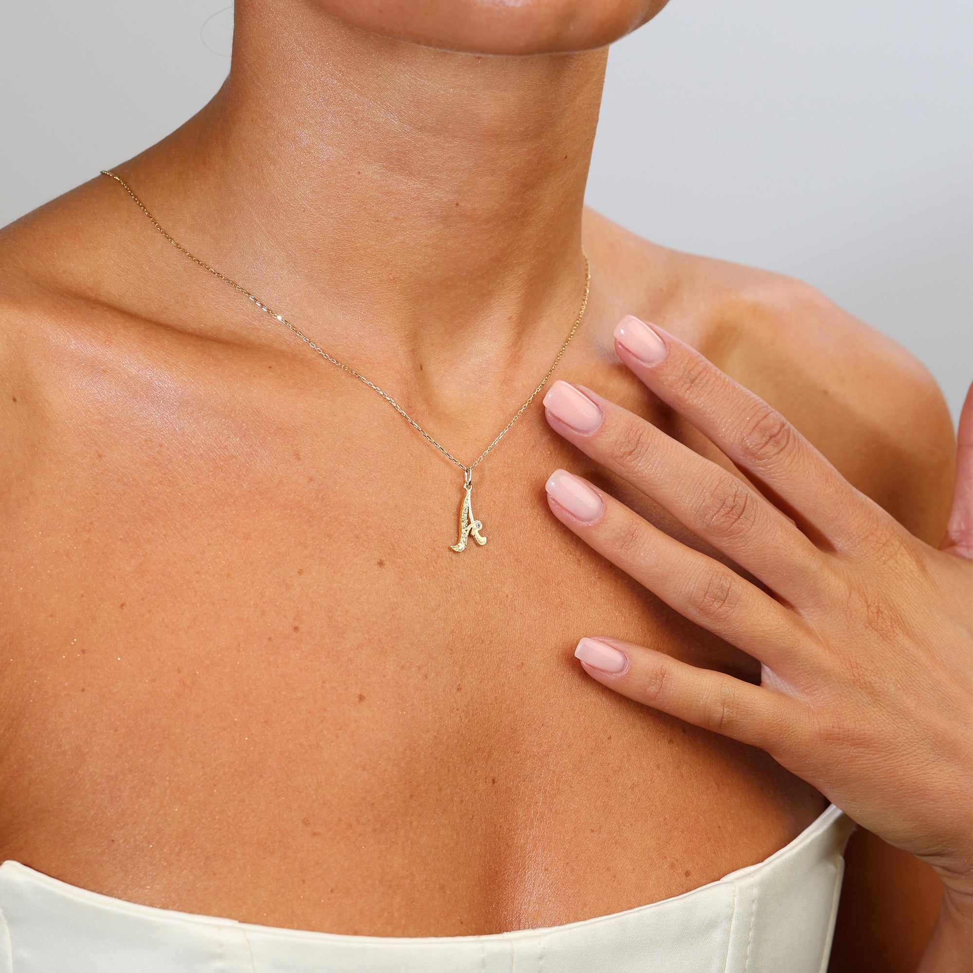 Gold necklace with a letter 'A' pendant worn by a person, with a hand touching the neck.