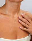 Gold necklace with a letter 'A' pendant worn by a person, with a hand touching the neck.