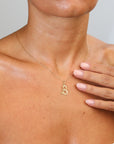 Gold necklace with a 'B' pendant worn by a person, with a hand touching the shoulder.