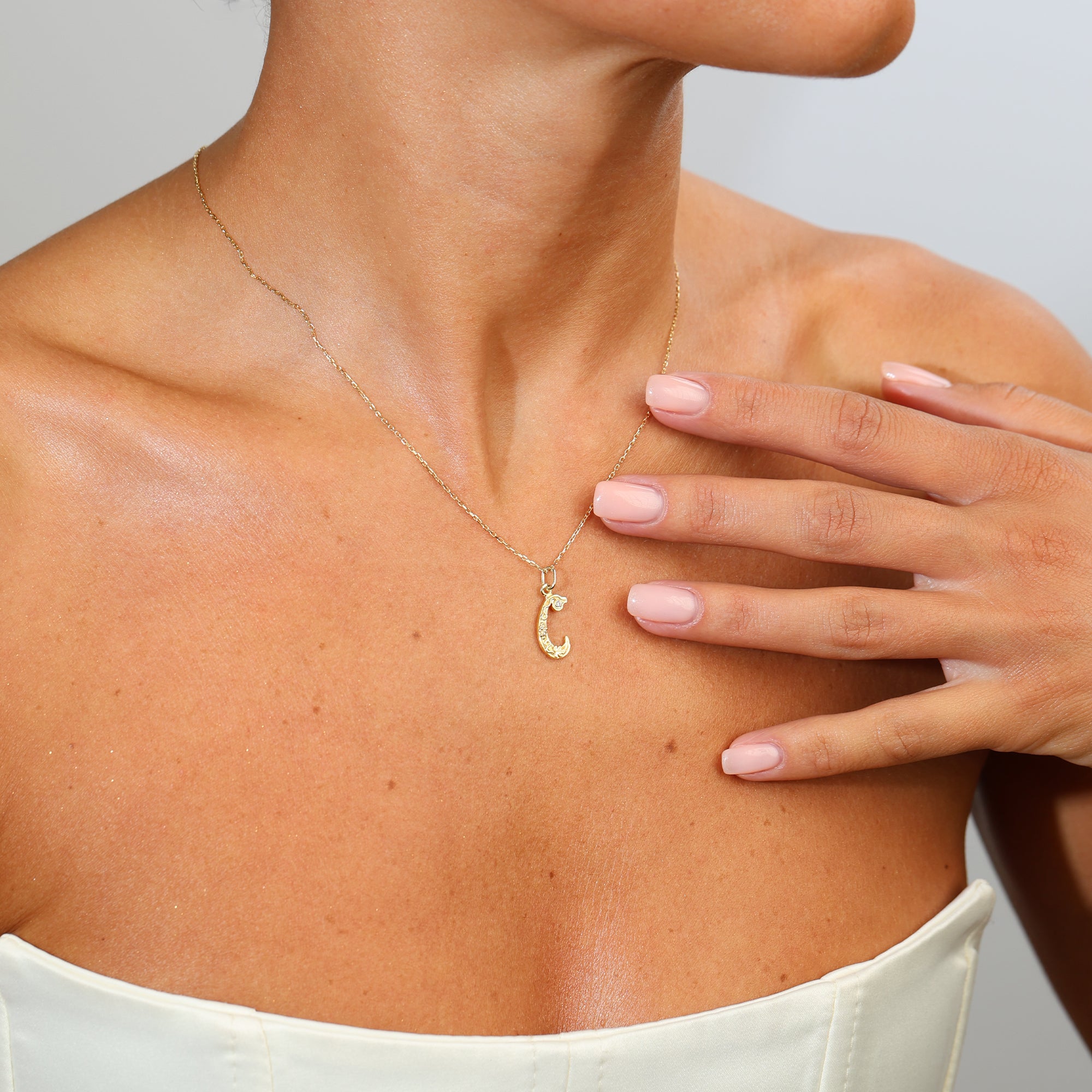 Gold necklace with a 'C' pendant worn by a person, with a hand touching the chest.