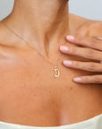 Gold necklace with a 'D' pendant worn by a person, with a hand touching the neck.
