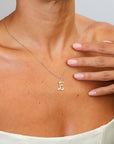 Gold necklace with a letter 'E' pendant worn by a person, with a hand touching the neck.