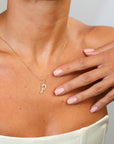 Gold necklace with a letter 'P' pendant on a person's neck with a hand touching their shoulder.
