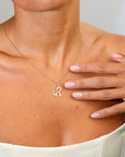 Gold necklace with a letter 'R' pendant worn by a person with a hand on their chest.