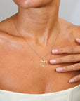Gold necklace with a pendant worn by a person, with a hand touching the chest.