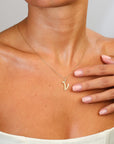 Gold necklace with a 'V' pendant worn by a person, with a hand touching the chest.