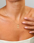 Gold necklace with a letter 'Z' pendant worn by a person, with a hand touching the chest.