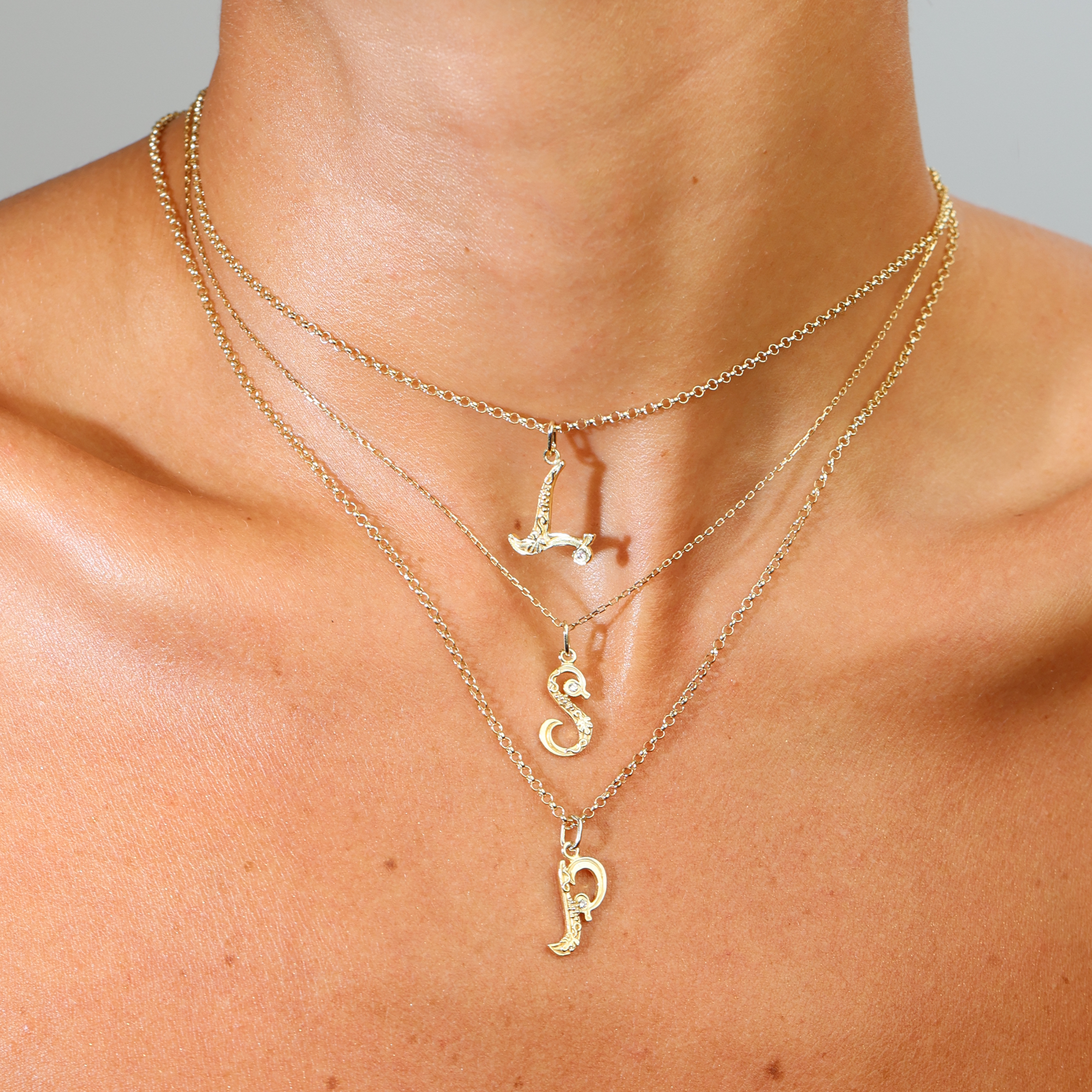 Gold necklaces with letter pendants on a person's neck against a neutral background
