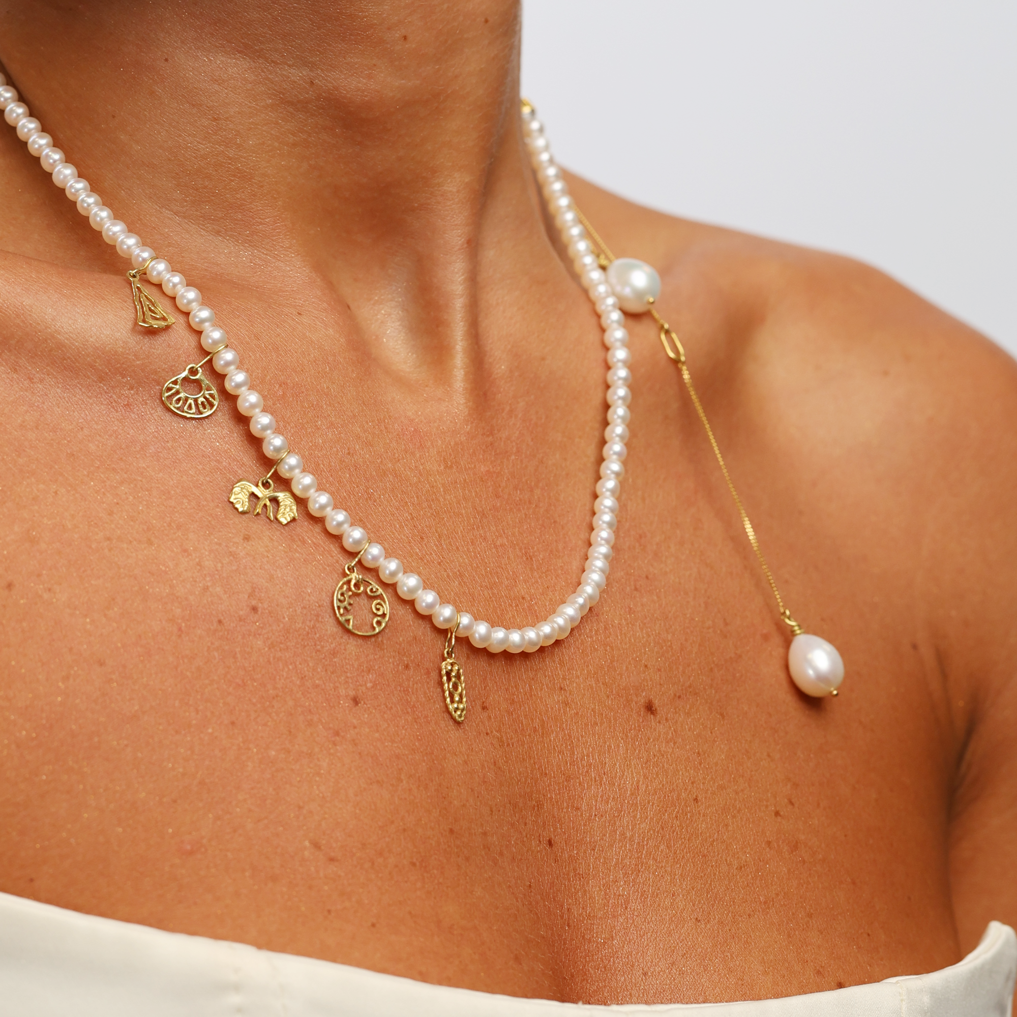 Pearl necklace with gold charms on a person against a neutral background