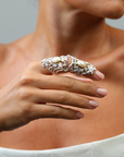 Close-up of a hand wearing a decorative armor ring with pearls against a neutral background
