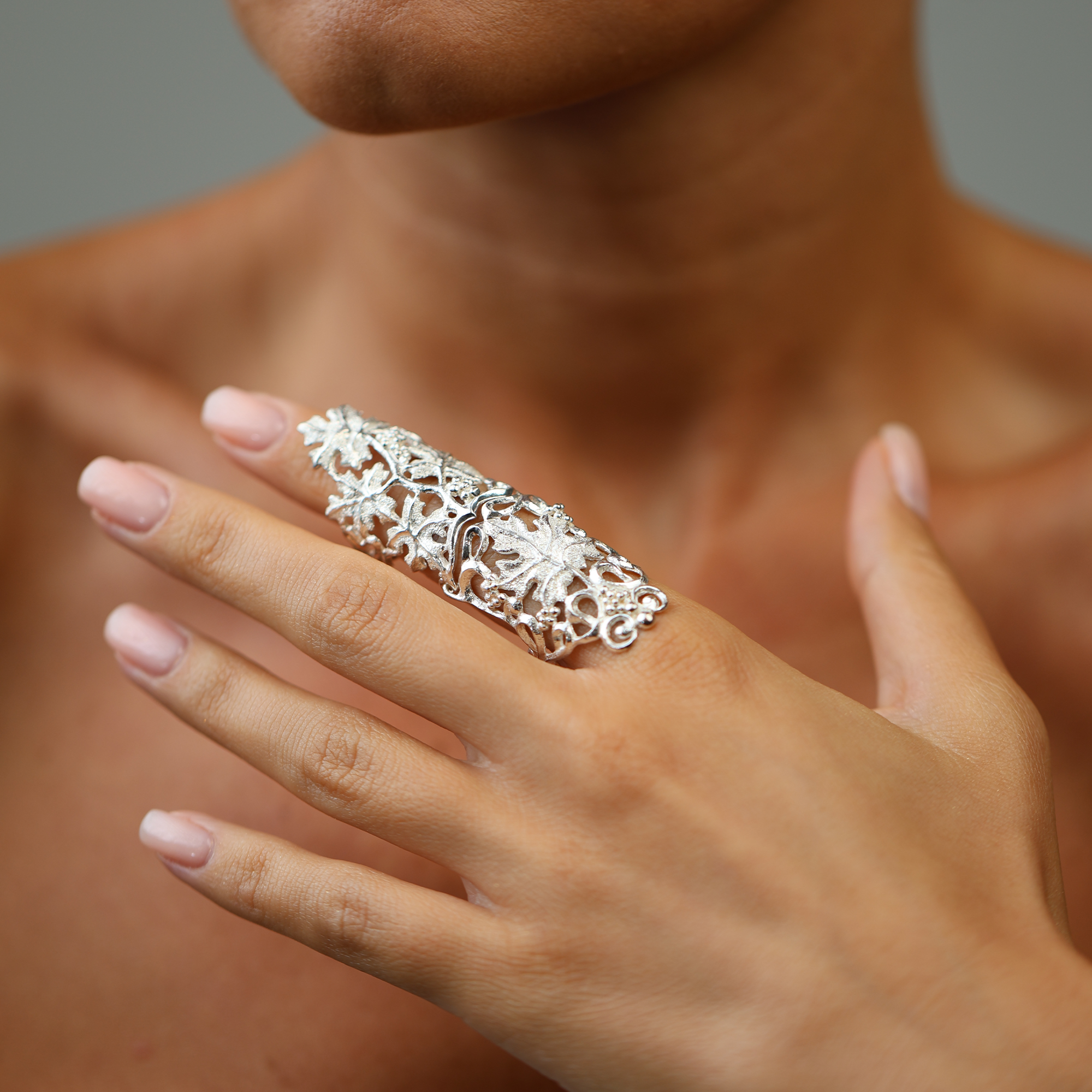 Close-up of a hand wearing an ornate silver ring against a neutral background