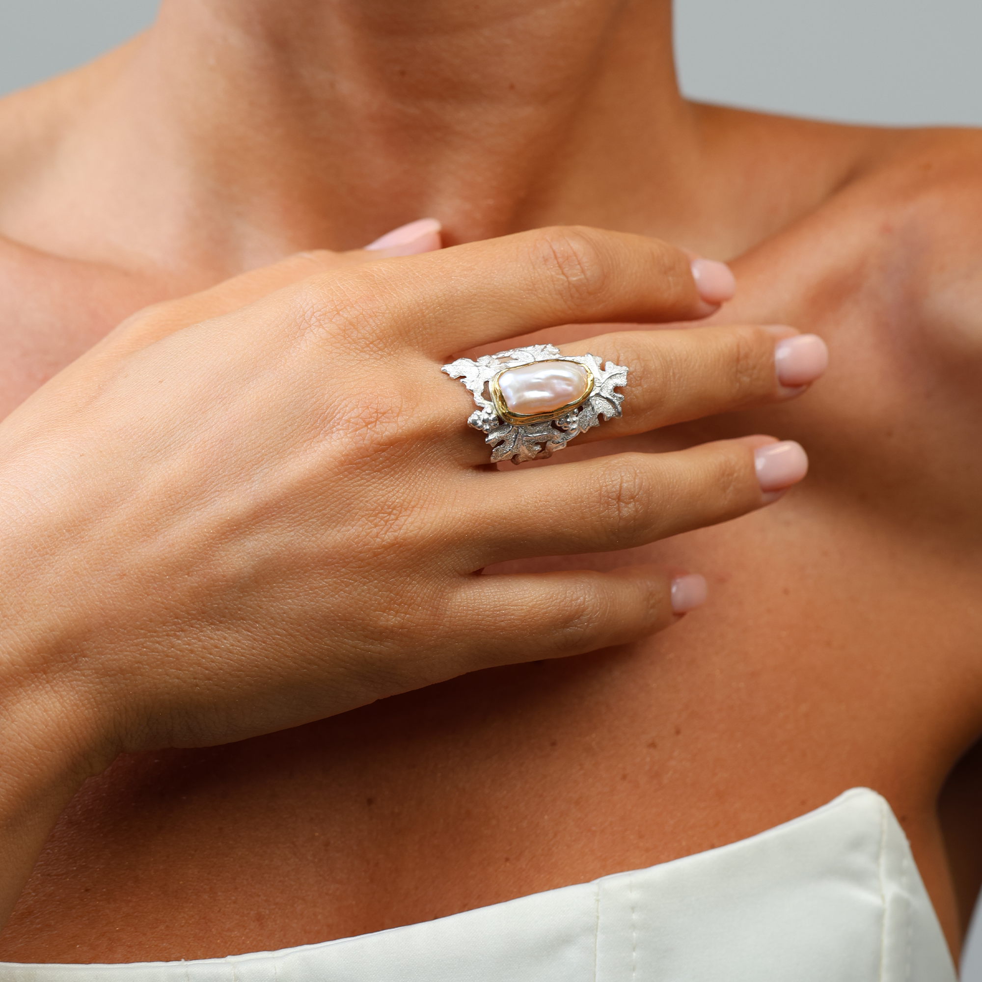 Close-up of a hand wearing an ornate ring with a large central gemstone, set against a neutral background.