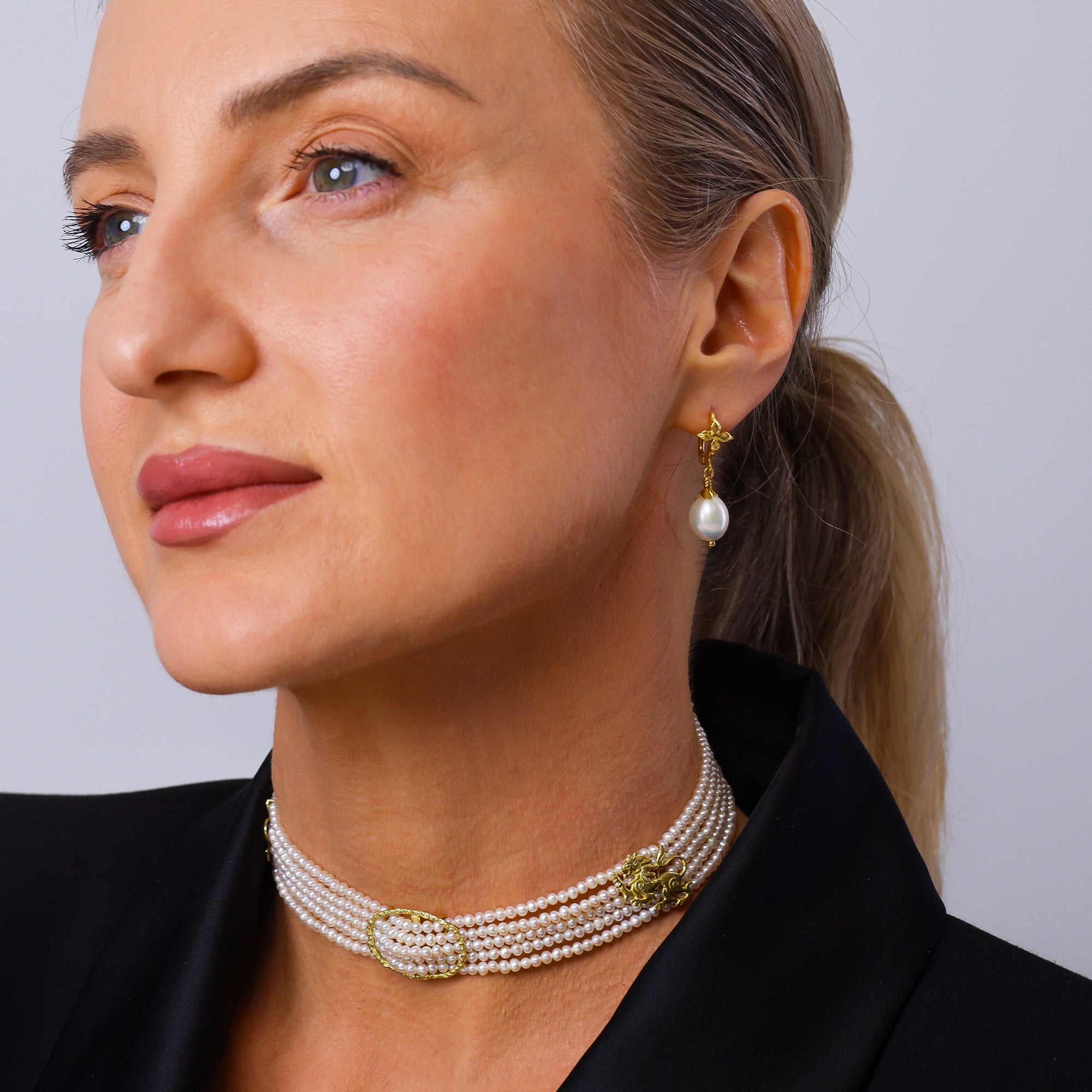 Close-up of a woman wearing a pearl necklace and earrings against a plain background